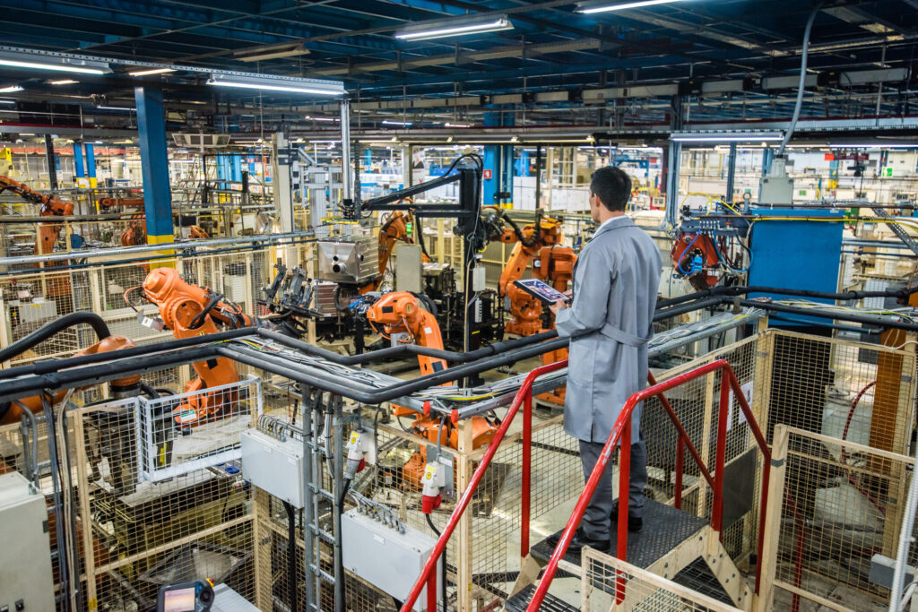 An employee overseeing robotic manufacturing operations from an elevated walkway.